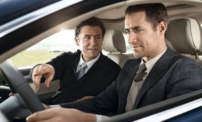 one businessman is pointing to the car dash while speaking to another businessman